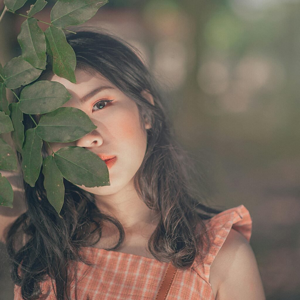 Close-up of a woman in a summer dress, partially hidden by leaves, outdoors.