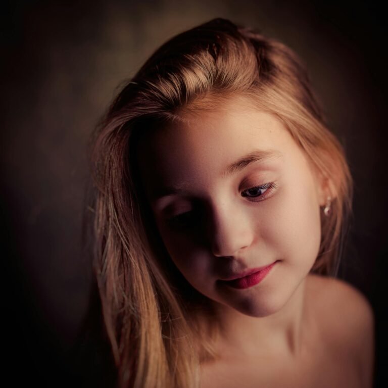 Tender portrait of a young blonde girl with an introspective pose in soft lighting.